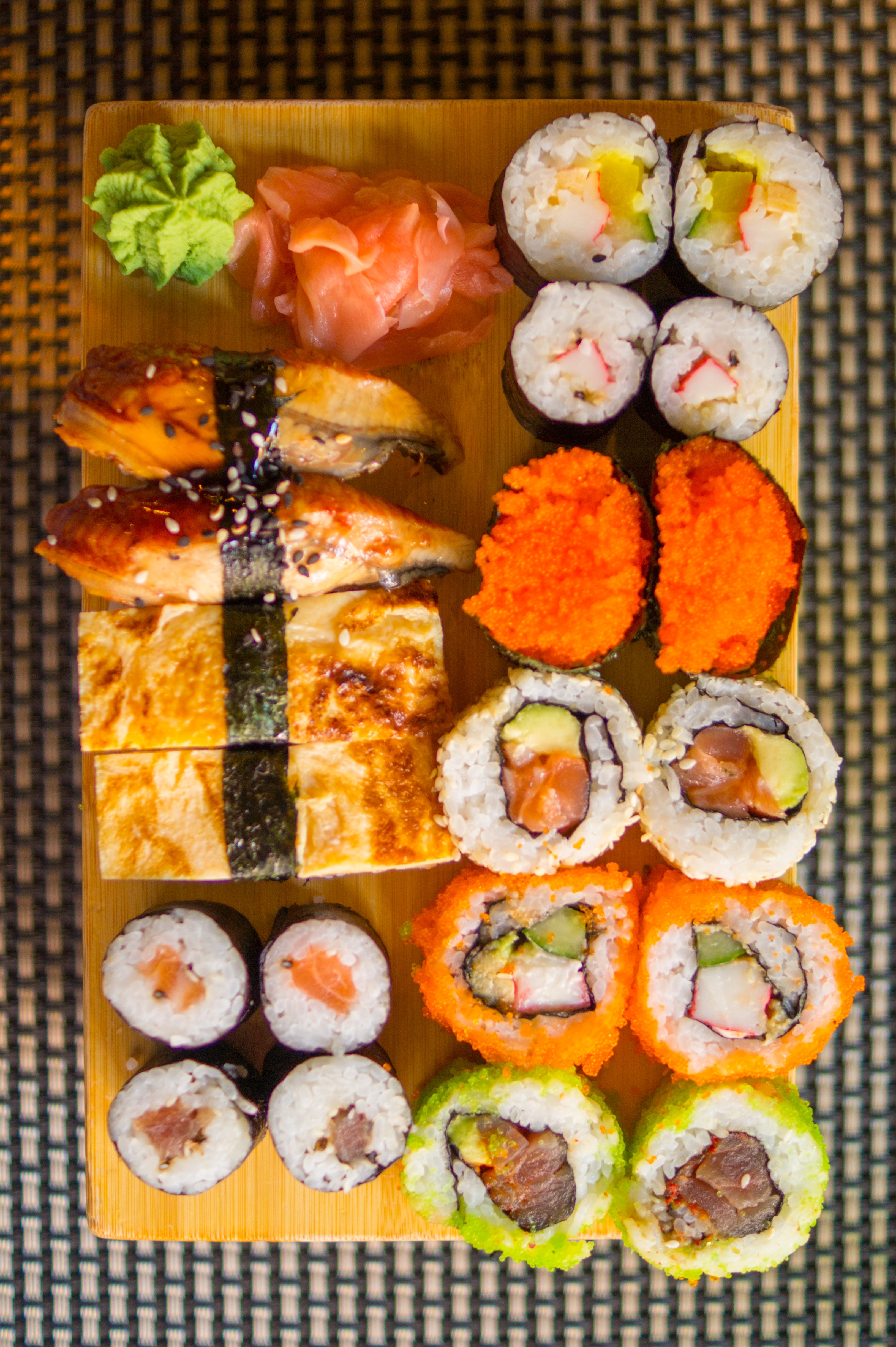 Na zdjęciu sfotografowane zostało typowe japońskie jedzenie czyli sushi.Na prostokątnym żółtym talerzu ułożone są 4 kolumny przysmakó zrobionych z ryżu i ryb. Większość ma kształt okrągłego koreczko z kropką w innym kolorze na środku. Jednak na talerzu możemy zauważyć również jasnozielony kleks kremu, podłużne i kwadratowe zakąski. Całość wygląda kolorowo.